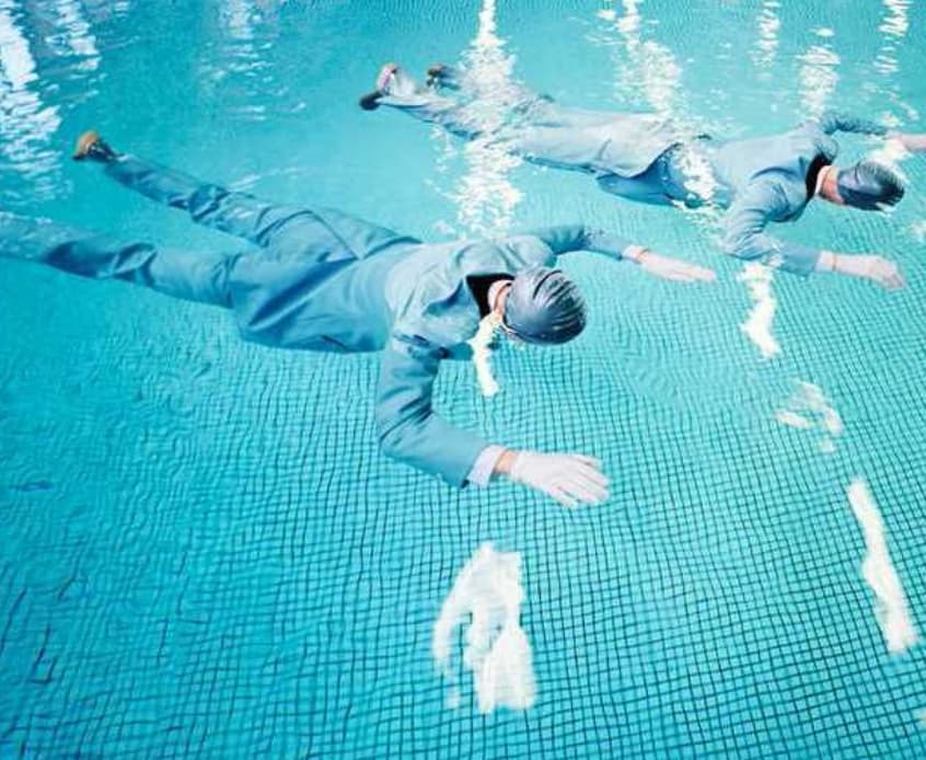 Two people swimming underwater in business suits