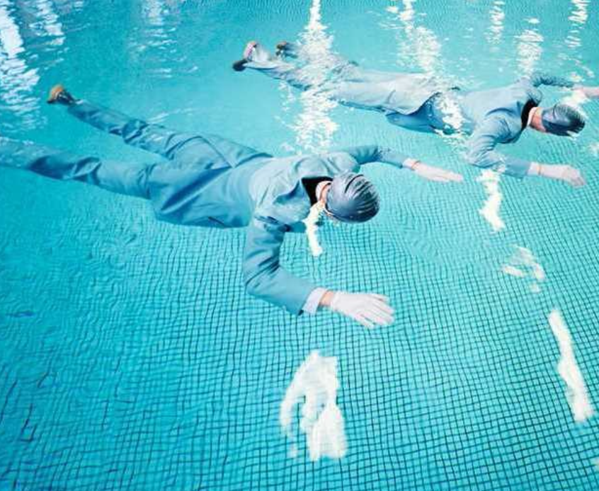 Two people swimming underwater in business suits